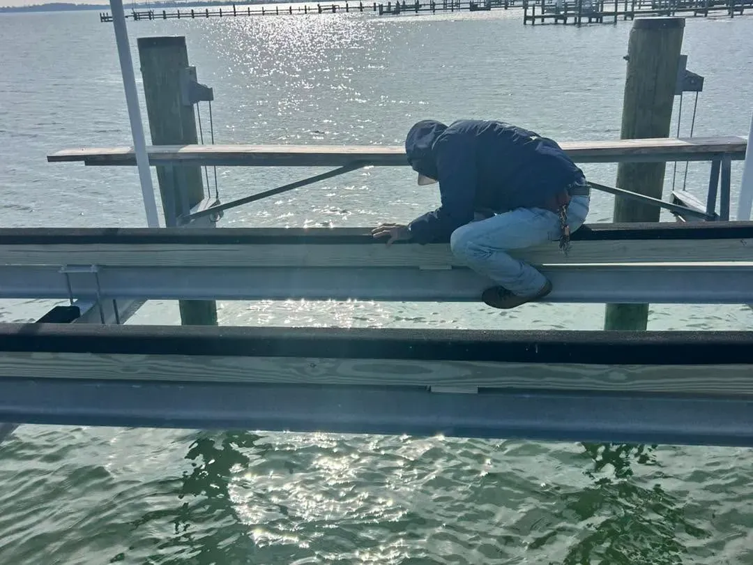 Technician kneeling on a boat lift cradle over the river